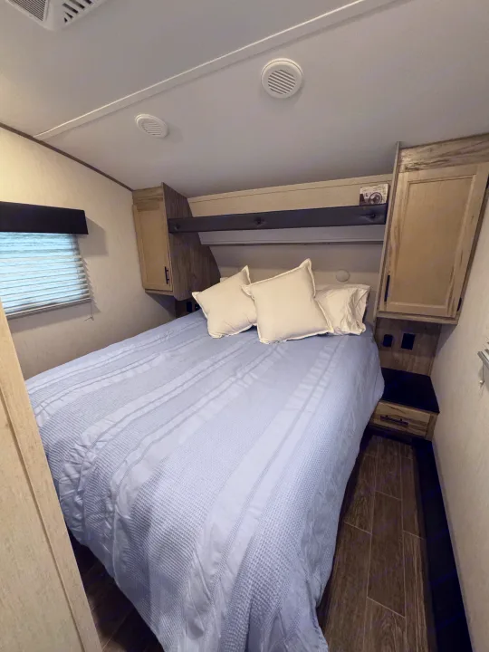 Comfortable RV rental bedroom with a bed, blue patterned comforter, nightstands, overhead storage, and window.. Forest River Cherokee Arctic Wolf 2022