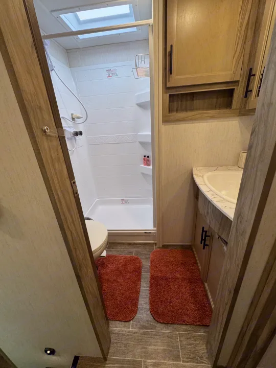 Compact rv rental bathroom featuring a white shower, toilet, and wooden vanity with a sink.. Forest River Cherokee Arctic Wolf 2022