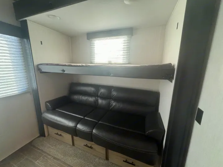 Spacious RV rental interior featuring a bunk bed above a black leather sofa with storage drawers.. Forest River Cherokee Arctic Wolf 2022