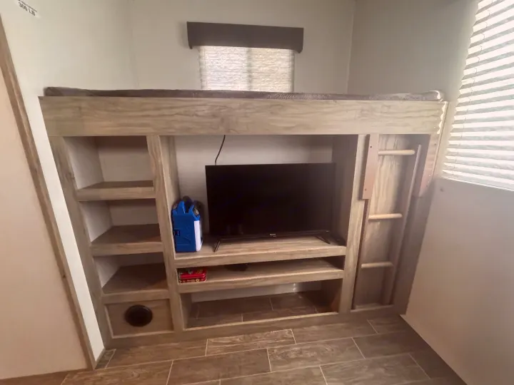 This RV rental features a lower entertainment center with TV & shelves beneath a top bunk bed, accessible by a ladder.. Forest River Cherokee Arctic Wolf 2022