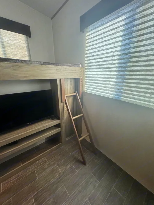 RV rental interior featuring a built-in bunk bed with ladder, a TV console, window with blinds, and wood-look tile flooring.. Forest River Cherokee Arctic Wolf 2022