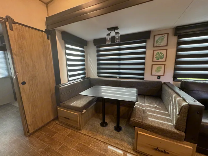 Cozy RV rental dinette area featuring modern striped blinds, built-in storage, and leafy wall art, with sunlight streaming in.. Forest River Cherokee Arctic Wolf 2022