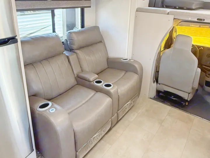 Step into comfort! This RV rental offers a cozy interior with brown recliners, cup holders, a fridge, and the front cab area.. Forest River Coachmen Freelander 2023
