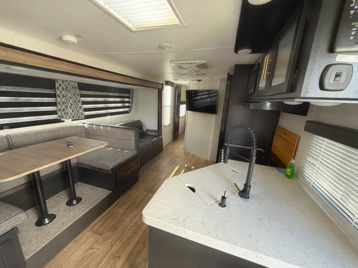 Inside this modern rv rental: a cozy dinette, well-equipped kitchen, and lounge area with sleek wood floors.. Forest River Cherokee Grey Wolf 2022