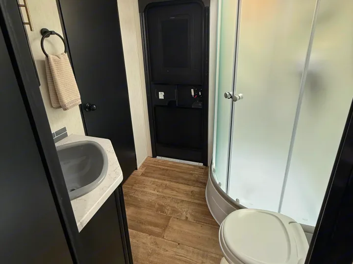 Compact RV rental bathroom featuring a gray sink, dark cabinetry, frosted shower, and white toilet.. Forest River Cherokee Grey Wolf 2022