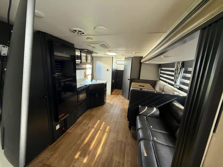 Modern rv rental interior with sleek kitchen, dinette, and sofa, brightened by sunlight on the wood-look floor.. Forest River Cherokee Grey Wolf 2022