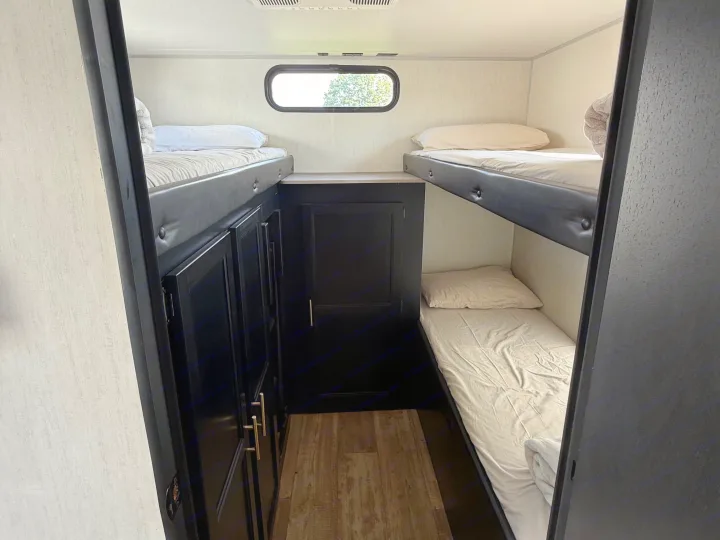 RV rental bunkhouse with four beds, including two bunk sets. Features a window, central storage, and wood-patterned floor.. Forest River Cherokee Grey Wolf 2022