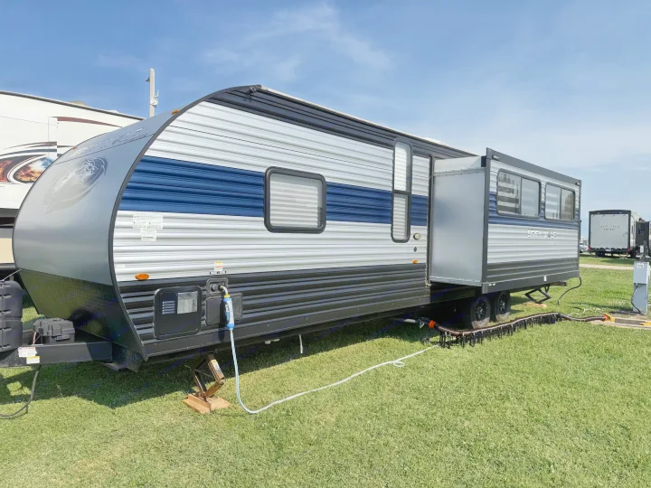 This blue and grey travel trailer RV rental is fully set up at a sunny campsite with hookups and an extended slide-out.. Forest River Cherokee Grey Wolf 2022