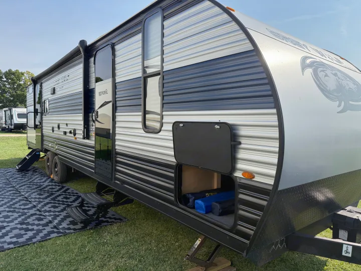 This Grey Wolf travel trailer RV rental, parked on grass with its storage open, offers a perfect camp setup.. Forest River Cherokee Grey Wolf 2022