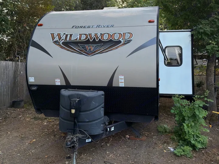 Forest River Wildwood travel trailer RV rental, front view. Features an extended slide-out, propane tanks, parked on dirt.. Forest River T27TDSS 2017