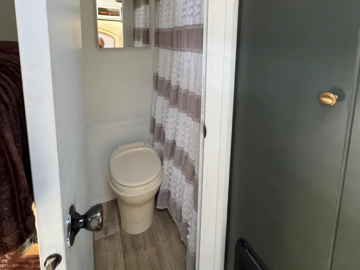 Compact RV rental bathroom with toilet, mirror, and striped shower curtain.. Sportsmen Classic 2014