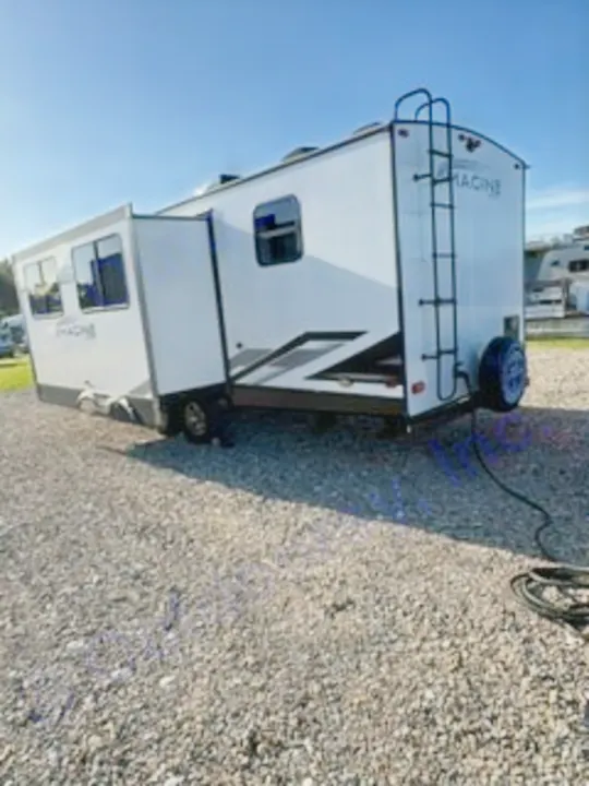 This Imagine travel trailer RV rental, with its slide-out extended, is parked on gravel, ready for your next trip.. Grand Design Imagine 2023