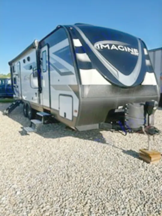 This sleek black and white Imagine travel trailer RV is available for rv rental, parked on gravel with its steps down and awning out.. Grand Design Imagine 2023