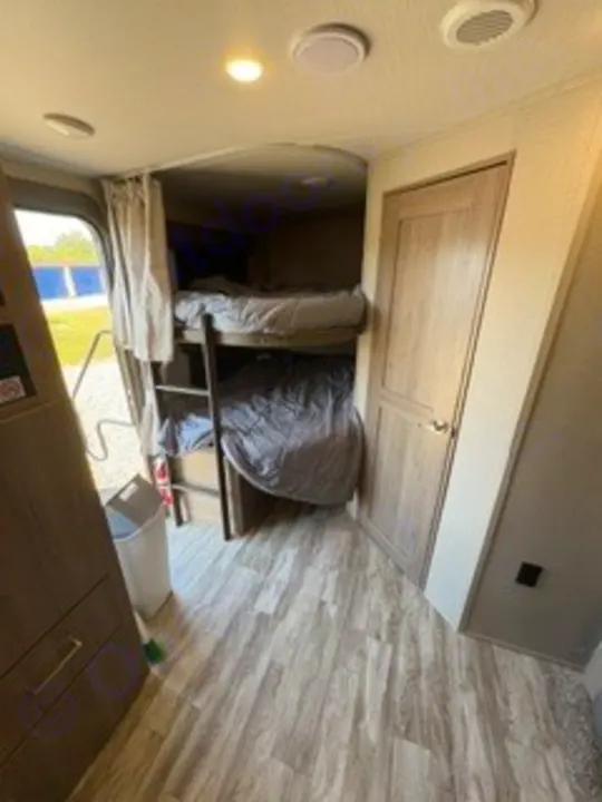 This RV rental's interior shows stacked bunk beds with a ladder, wood-look floor, and a door on the right for privacy.. Grand Design Imagine 2023
