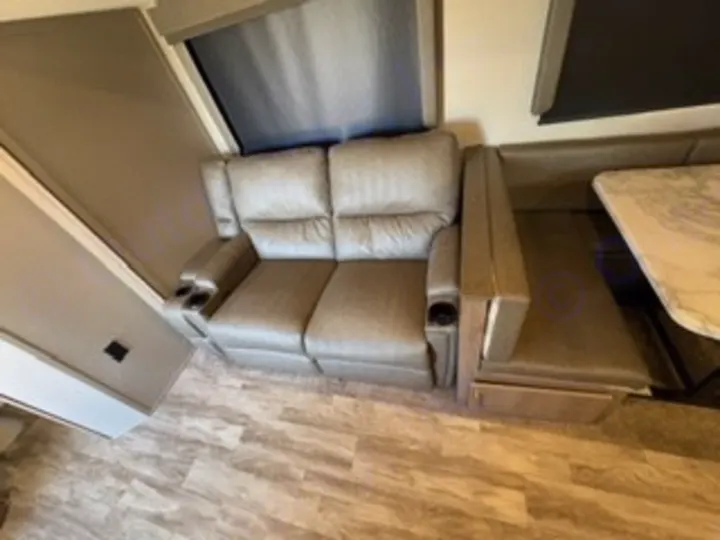 **RV rental** living space: A light gray reclining sofa with cupholders sits next to a dinette bench and marble-look table.. Grand Design Imagine 2023