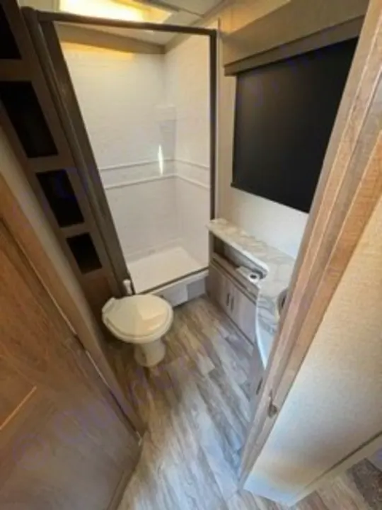Clean RV rental bathroom featuring a toilet, glass shower, vanity, and window with blind. Your comfy adventure awaits!. Grand Design Imagine 2023
