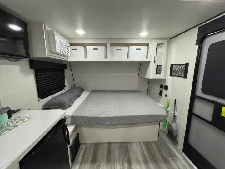 Clean rv rental bedroom with a comfy bed, AC, overhead storage, mini-fridge, and broom, optimized for small spaces.. Jayco Jay Flight SLX Sport Edition 2026