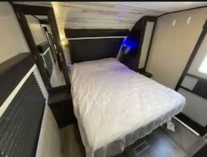 Inside an RV rental! Comfortable travel trailer bedroom features a queen bed, nightstands, and a full-length mirror.. Jayco White Hawk 2021