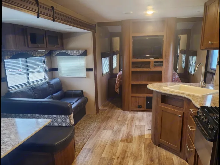 Inside this rv rental, view the living area with a dark sofa, dining booth, kitchen with sink, and entertainment center.. Aspen Trail Aspen Trail Trailer 2018
