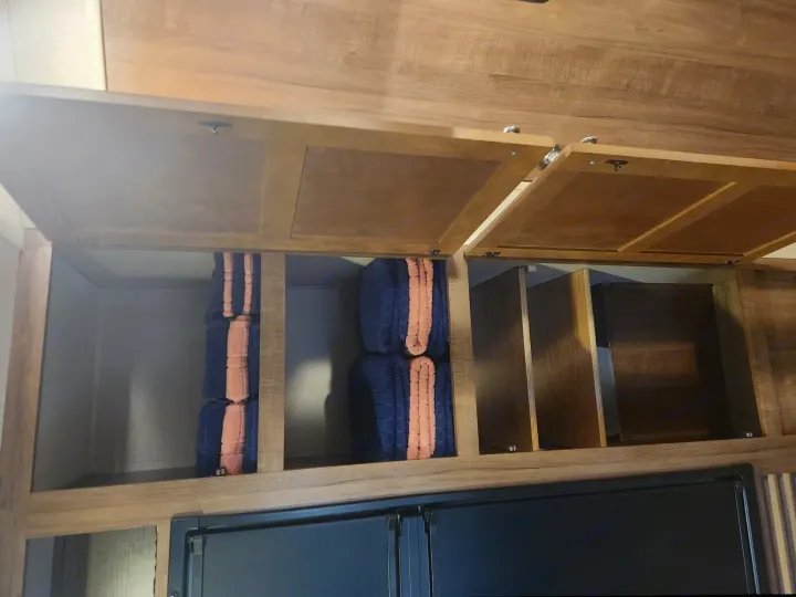Open overhead cabinets in an RV rental show blue & orange towels, empty shelves, & a dark appliance below for organized storage.. Aspen Trail Aspen Trail Trailer 2018