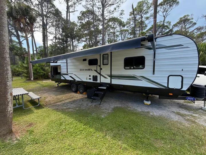An Eddie Bauer RV rental parked at a lush campsite, featuring an extended awning & outdoor setup. Ideal for camping.. Heartland RVs Eddie Bauer 2026