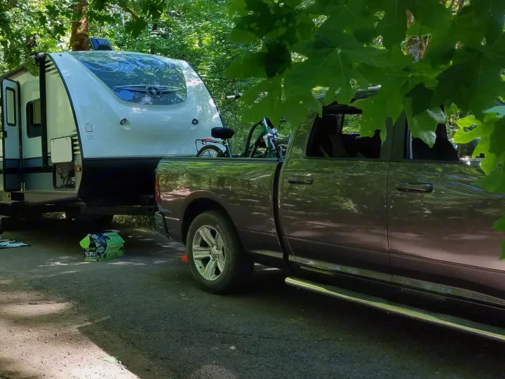 Camping trip with an RV rental: a woman walks past a travel trailer and pickup truck in a sunny, green campground.. Forest River Surveyor 2018