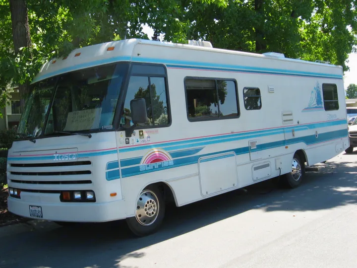 A white and blue 1993 Itasca Sunrise 31-ft Class A motorhome for sale, suitable for an rv rental fleet, parked on a street.. Itasca Sunrise 1993