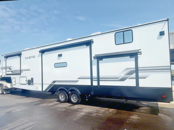 Side view of a modern white and black Sabre fifth-wheel RV rental, featuring multiple awnings and storage. Ready for your trip.. Forest River Sabre - 36DBB 2027