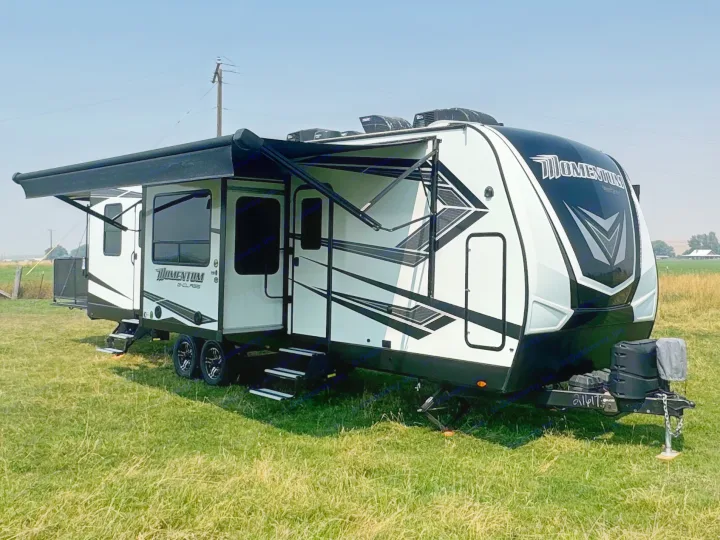 This sleek white and black Momentum G-Class RV rental, parked in a grassy field with awnings out, is ready for adventure.. Grand Design Momentum 2022