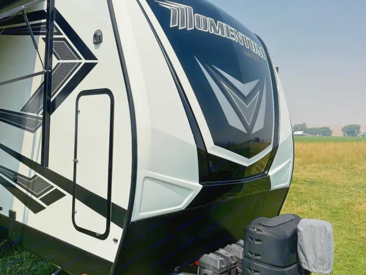 Detail of a sleek white and black Grand Design Momentum RV rental, showcasing its modern exterior in a grassy field.. Grand Design Momentum 2022