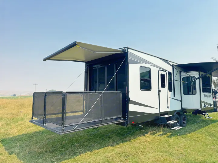 White & black travel trailer RV rental with deployed awnings and a rear patio deck, set in a sunny grassy field.. Grand Design Momentum 2022