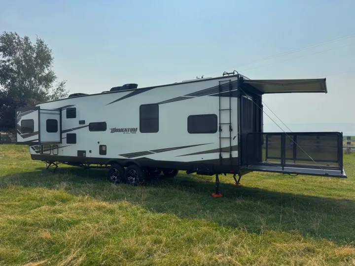 This large RV rental, a Momentum G-Class toy hauler, is parked in a sunny field with its deck and awning out.. Grand Design Momentum 2022