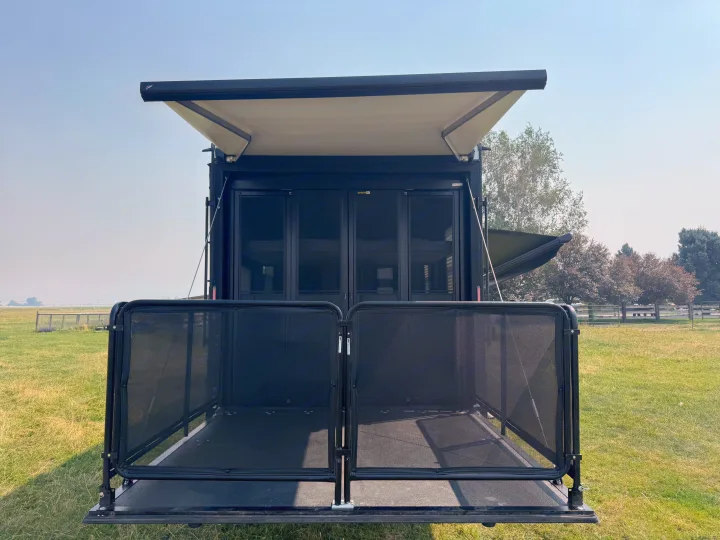 Black toy hauler RV rental with its patio ramp and extended awning in a grassy field, ideal for outdoor living.. Grand Design Momentum 2022