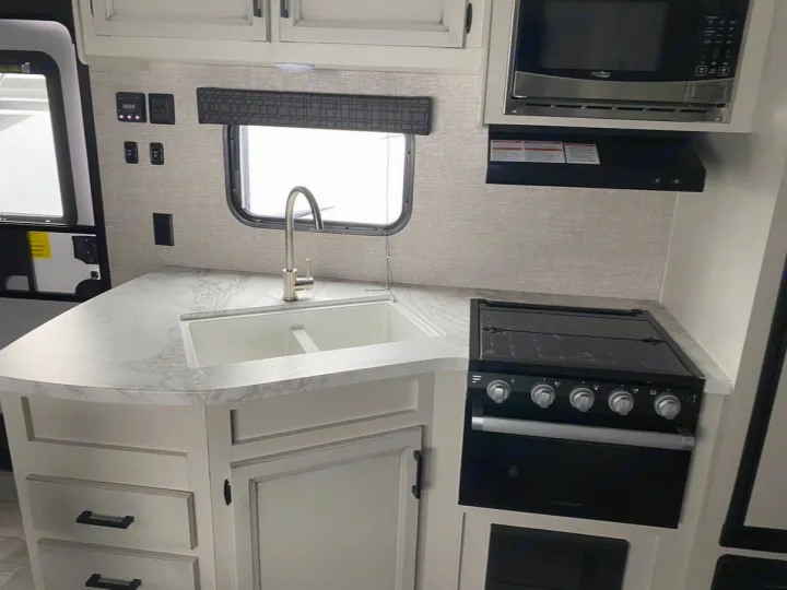 Bright RV rental kitchen featuring a sink, microwave, stovetop/oven, light cabinets, and a marbled countertop.. Jayco Jay Flight SLX 2022
