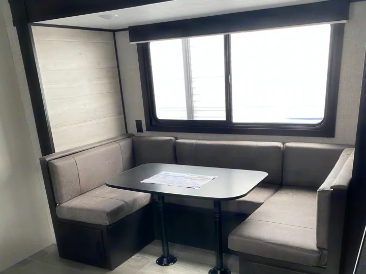 RV rental dinette with U-shaped booth seating, a black table, and a large window providing ample natural light.. Jayco Jay Flight SLX 2022