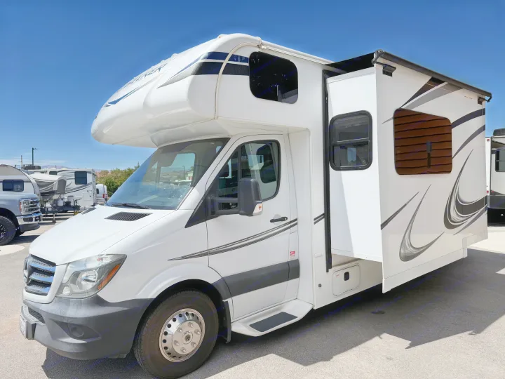 A white Class C motorhome rv rental with its slide-out extended, parked on asphalt under a clear blue sky.. Forest River Sunseeker MBS 2018