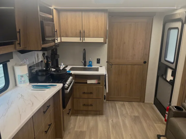 Spacious RV rental kitchen with microwave, stovetop, sink, and ample counter space for cooking on the road.. Grand Design Imagine XLS 2024