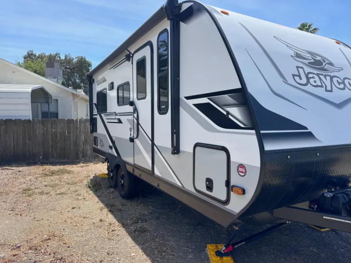 Modern Jayco Jay Feather RV rental parked on gravel. White/black exterior with awning extended, ready for your next adventure.. Jayco Jay Feather 2025