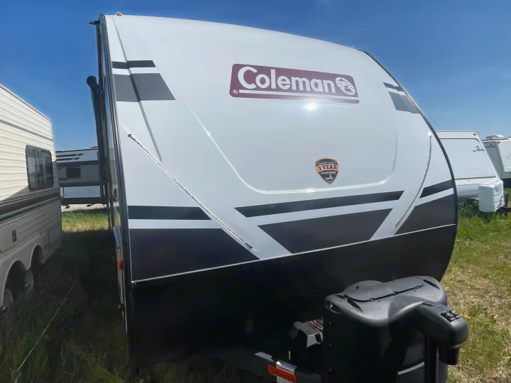 This white and black Coleman travel trailer, an excellent RV rental option, sits ready in an outdoor lot.. Dutchmen Coleman Light 2022