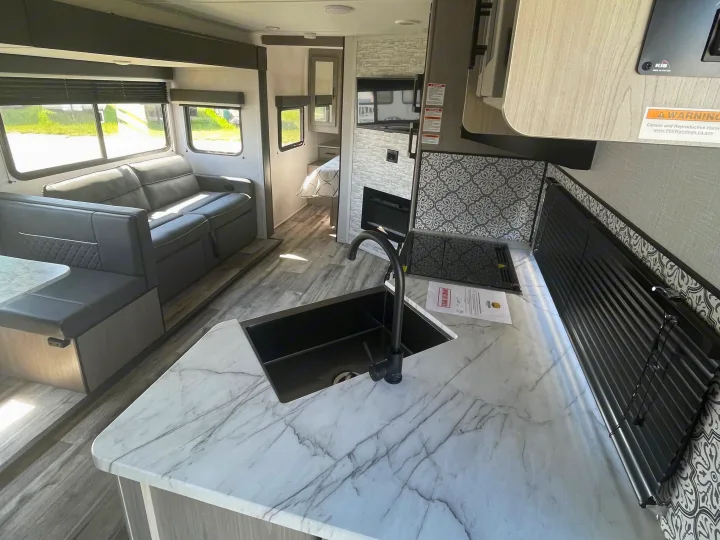 Modern RV rental interior: Kitchen with marble counters, black sink, and a view of the spacious living and dining area.. Dutchmen Coleman Light 2022