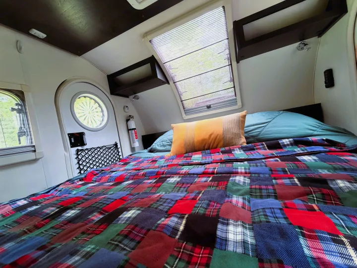 Cozy RV rental interior featuring a bed with a vibrant patchwork blanket, windows, and a fire extinguisher for safe travel.. nuCamp T@G 2022