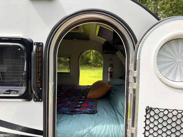 Cozy Boulder teardrop RV rental interior with a comfy bed, fire extinguisher, and a refreshing nature view through the window.. nuCamp T@G 2022