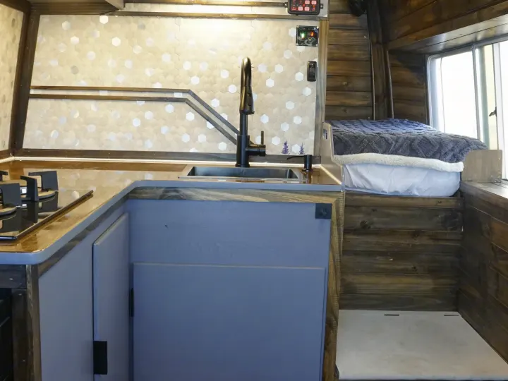 Cozy RV rental interior featuring a kitchenette with sink and stove, wood paneling, and a comfy bed for your adventure.. Dodge Sprinter 2006