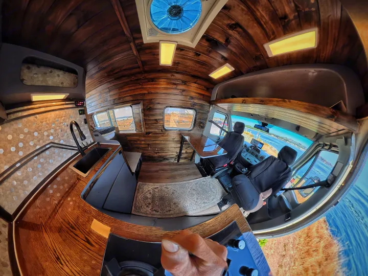 Inside a custom **rv rental**: wood-paneled ceiling, kitchenette with hexagonal tiles, driver's cabin, and water views. Hand adjusts controls.. Dodge Sprinter 2006