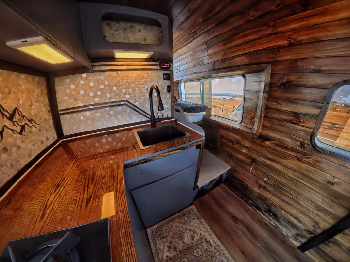 Step inside this charming RV rental featuring a custom wood kitchen, sink, mountain mural backsplash, and scenic views.. Dodge Sprinter 2006