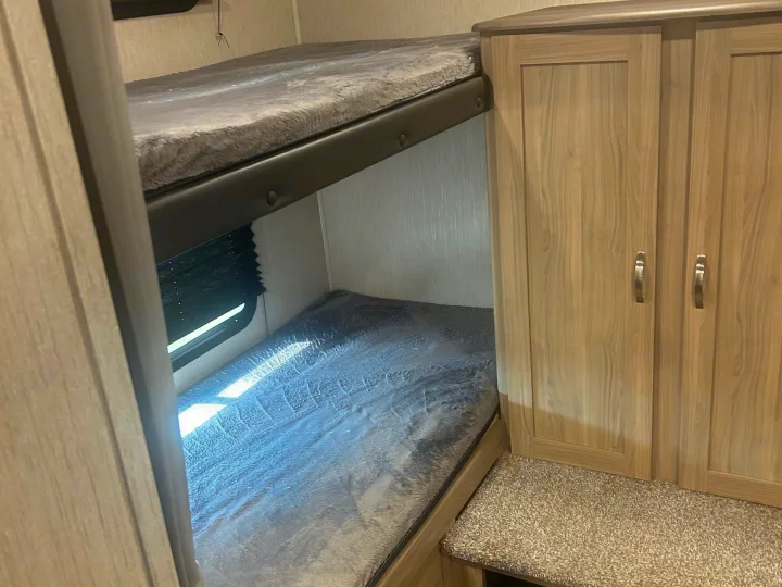Compact RV rental interior with cozy bunk beds and fuzzy grey bedding, alongside a light wood wardrobe.. Coachmen Freedom Express 2021