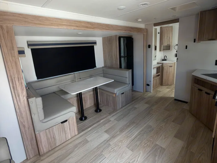 Spacious RV rental interior with a light wood-toned dinette, kitchen, refrigerator, and wood-look flooring.. Winnebago Access 2025