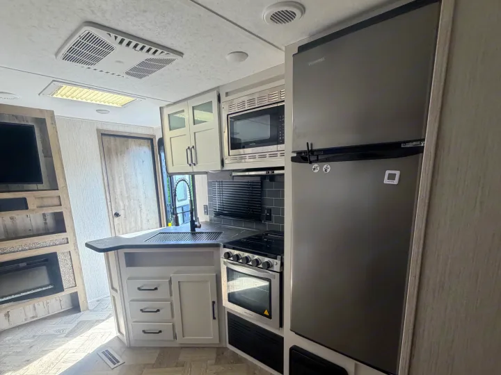 Modern RV rental kitchen with stainless appliances, sink, and nearby living space featuring a TV and fireplace.. Forest River Palomino Puma 2021