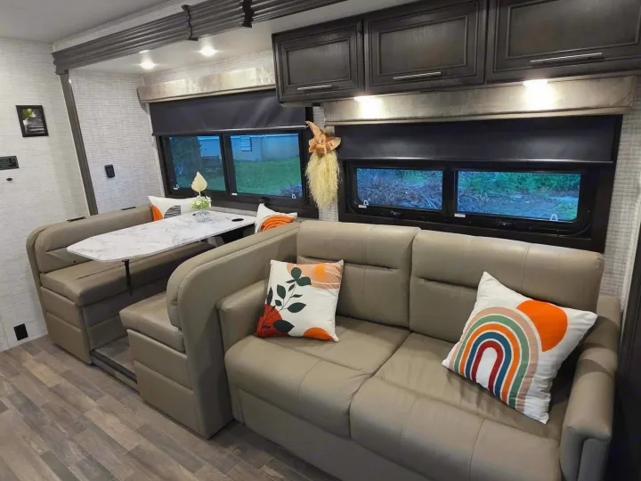 Spacious RV rental interior featuring a comfy sofa, dinette, wood-look flooring, and modern decor for a great mobile living experience.. Jayco Greyhawk 2024