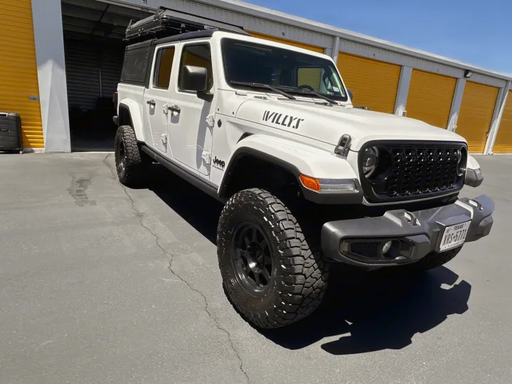 A white Jeep Gladiator with a rooftop tent, parked at storage units. Your ultimate RV rental for adventure travel.. Jeep Gladiator Willys 2024